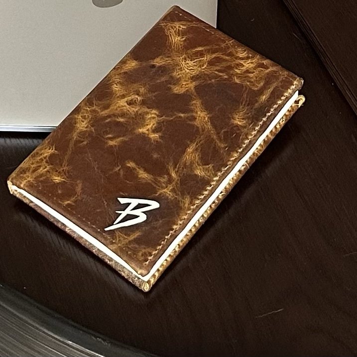 A stitched brown leather journal with a white B on the cover, on a dark surface